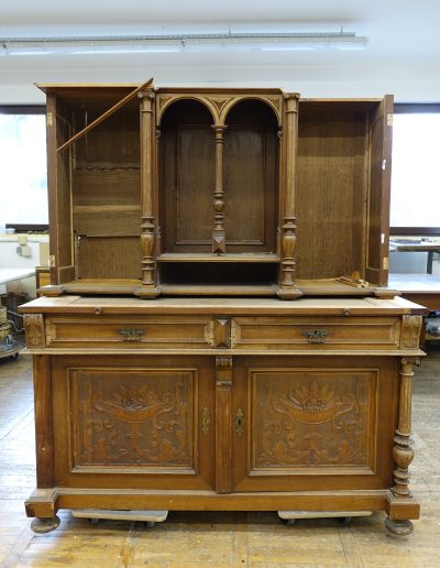 Omara pred kons.-rest. posegom Restavriranje smo začeli s fotodokumentacijo in razstavitvijo omare na posamezne elemente. Po dezinsekciji in dezinfekciji je sledilo grobo suho čiščenje ter odstranjevanje samolepilnih tapet, ki so kazile površino. Ohišje smo stabilizirali z obsežno mizarsko sanacijo, dopolnili manjkajoči nosilni les ter rekonstruirali močno poškodovane profilne letve in druge elemente. Močno uničene dele smo utrdili z injektiranjem in potapljanjem v sintetični utrjevalec, polomljene stebričke pa sestavili z lesenimi mozniki. Poškodbe zaradi insektov smo zapolnili z epoksidnim kitom in voskom. Dvignjen, odstopajoč ali poškodovan furnir smo ponovno prilepili, manjkajoče dele nadomestili z novimi furnirskimi vstavki, najbolj poškodovane površine pa ponovno furnirali. Izdelali smo manjkajoče profilne letve in stružene elemente, vključno z rekonstrukcijo celotnega stebra. Površino smo mehansko in kemično očistili, nove in stare elemente barvno uskladili ter jih zaščitili z izbranim površinskim premazom – voskom, oljem ali šelakovo polituro, skladno z dogovorom z naročnikom. Izvedli smo preventivno zaščito lesa, omaro ponovno sestavili, kovinsko okovje očistili in spolirali ter izdelali dva nova ključa. Zaključno smo poskrbeli za fotodokumentacijo pred, med in po posegu ter pripravili celovito poročilo. Omara je po temeljiti obnovi ponovno stabilna, estetsko izčiščena in pripravljena na novo življenjsko dobo – kot dragocen del notranje opreme ali kot razstavni eksponat. Konservatorsko-restavratorski poseg je bil izveden v letu 2023.